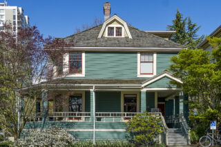 A 2-and-a-half asymmetrical Victorian home with a large porch, a hipped rooftop with a projecting dormer and a corbelled chimney