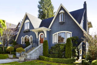 A blue, cream and red, single storey home with a steep roofline that almost reaches the floor, curving outwards (also known as a "cat slide" roof).