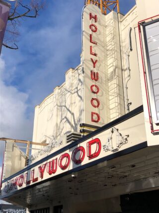 The exterior of a theatre building with a red-lettered sign on a white background reading 'Hollywood'.