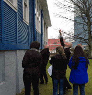 People standing in front of a blue and white heritage building with a sign 'Flying Angel Seafarers Club'.