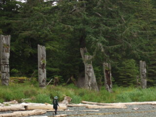 Rocky beach in foreground with large carved mortuary and memorial poles in background