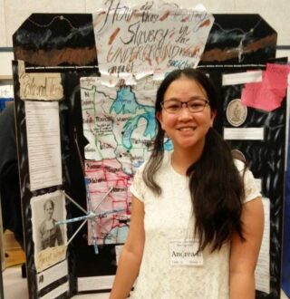 A student in front of her Heritage Fairs project at Heritage Hall in May 2022